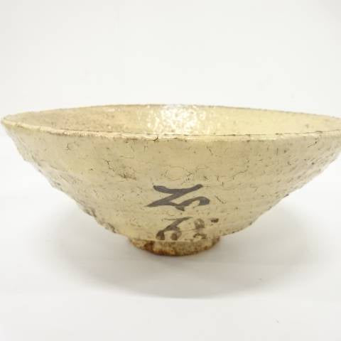 Front view of the Kaneko Sofu Hagi Ware chawan showing black calligraphic brushwork on a warm ivory speckled glaze.