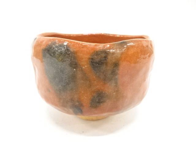 Front view of the Kawasaki Waraku Red Raku matcha bowl with warm red-orange glaze, charcoal-black markings, and a pale foot.