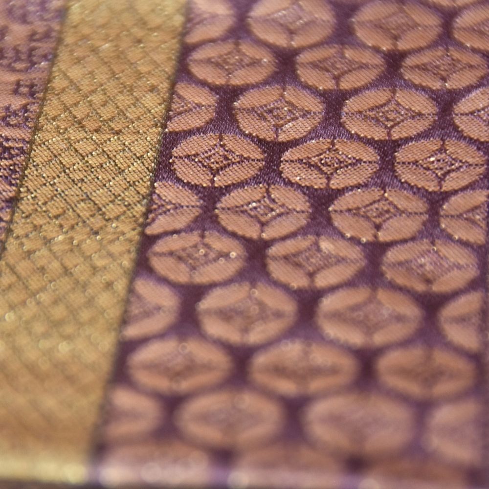 Close-up of textured fabric with a pattern, showing gold and purple colors.