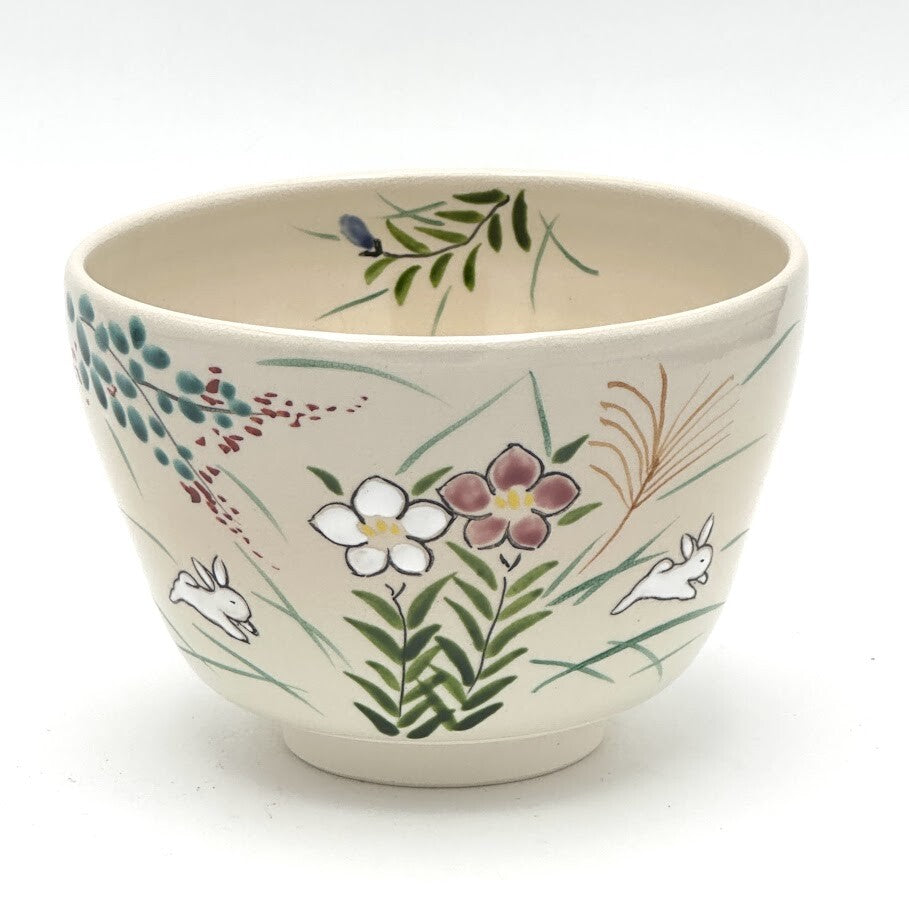 Hand-painted Kyo-yaki matcha bowl featuring the Akikusa ni Usagi motif with white rabbits, autumn grasses, flowers, and delicate green leaves on a warm ivory glaze