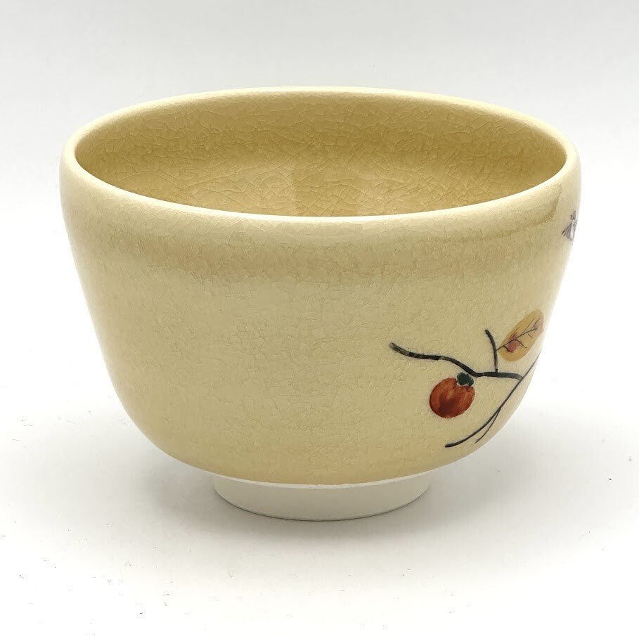 Side view of the hand-painted Kyo-yaki chawan showing a persimmon branch with autumn leaves and fruit against the warm beige glaze