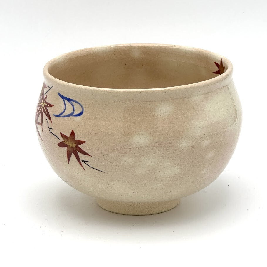 Angled view of the Kyo-yaki Momiji Ryusui chawan showing its rounded profile, warm beige glaze, and partial hand-painted maple leaf and flowing water motif