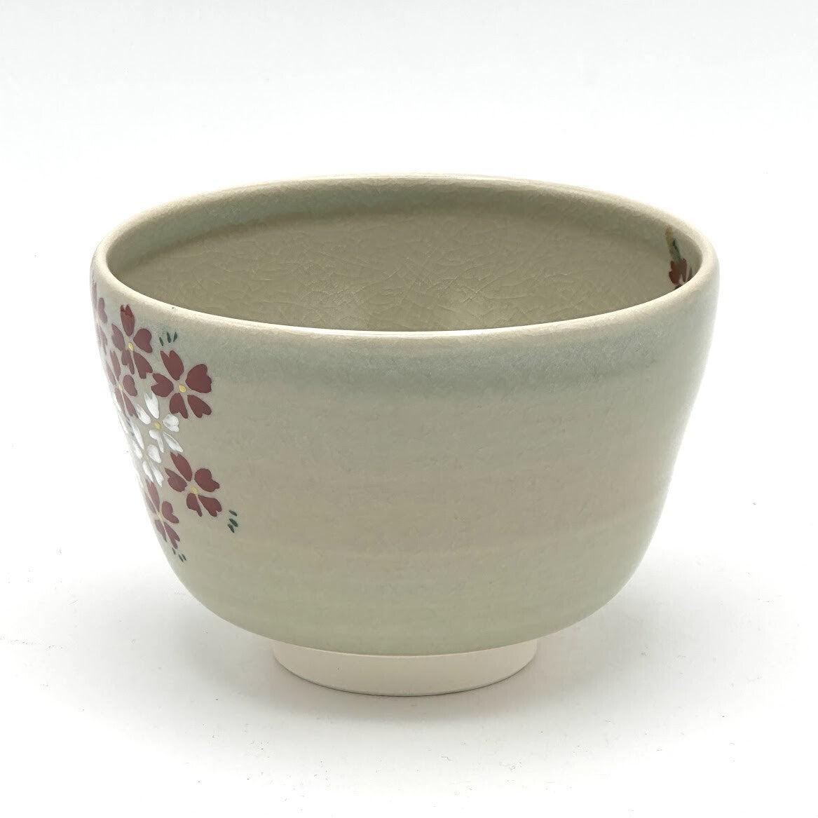 Angled view of the Kyo-yaki Sakurazume chawan showing its rounded profile, soft beige glaze, and partial hand-painted cherry blossom decoration