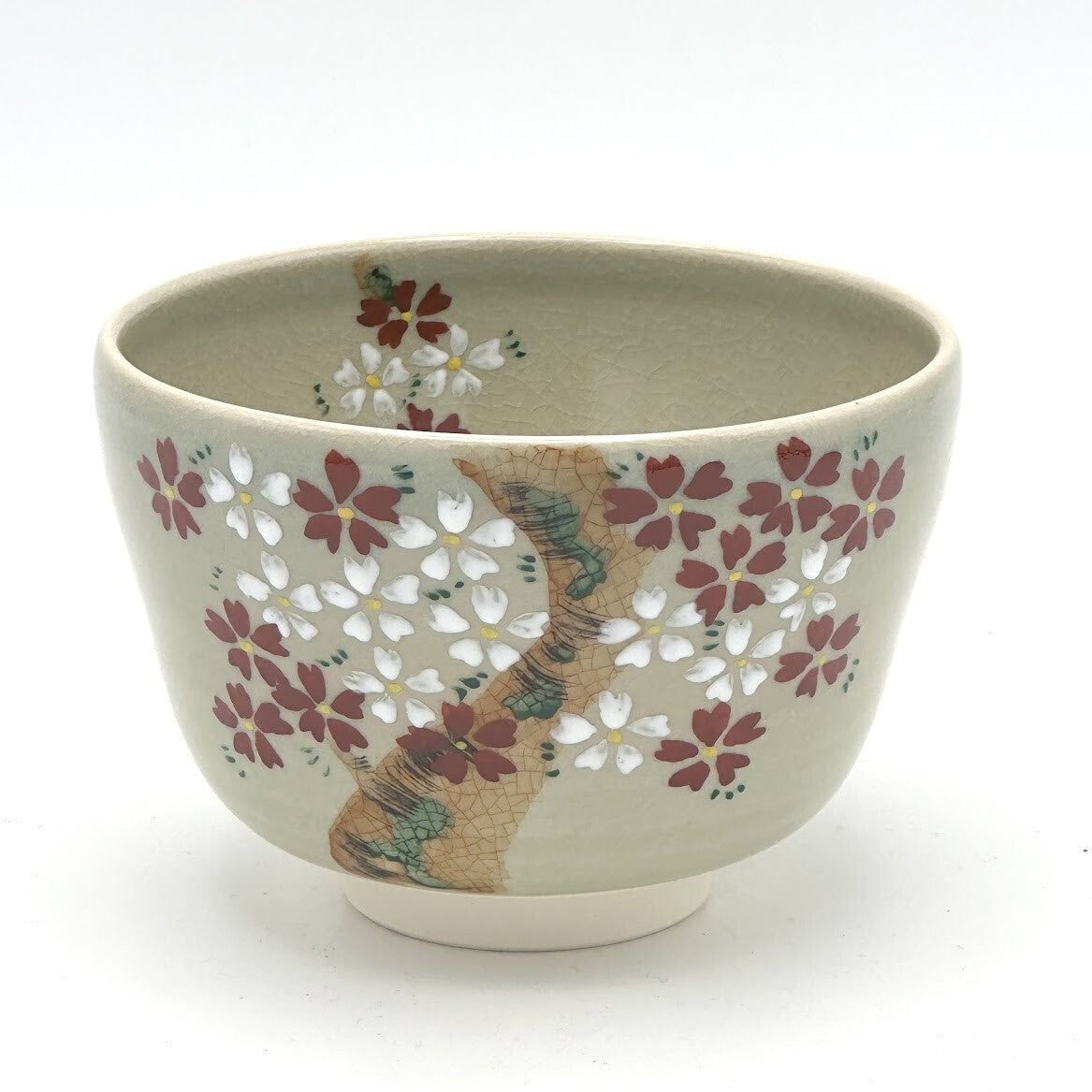 Hand-painted Kyo-yaki matcha bowl featuring the Sakurazume motif with dense pink and white cherry blossoms surrounding a textured tree trunk on a soft beige glaze