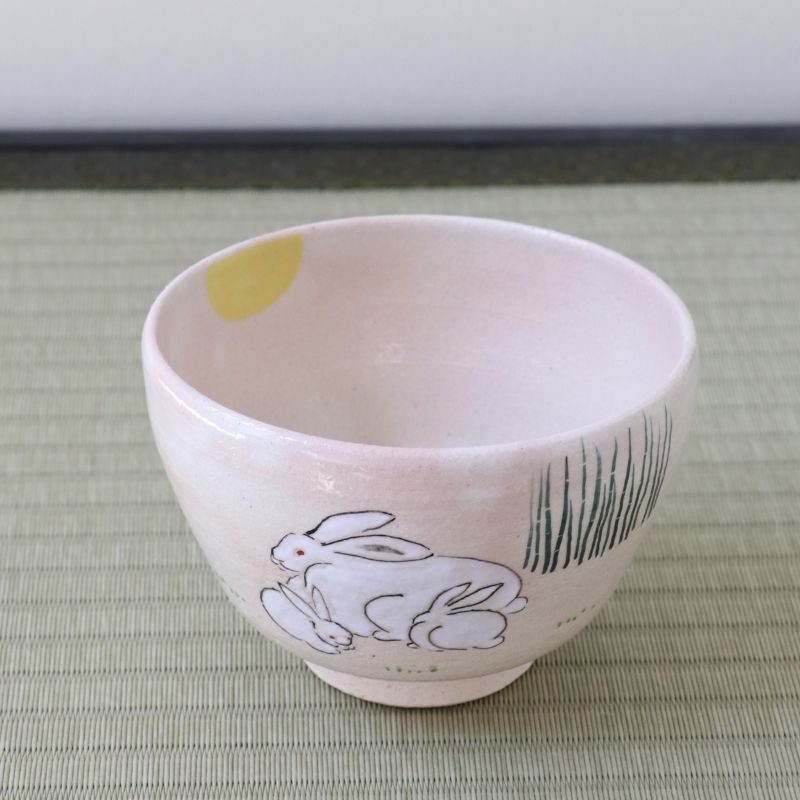 Angled view of the Kyo-yaki Tsukimi chawan showing the parent and child rabbits, yellow full moon, green grasses, and soft pink glazed interior