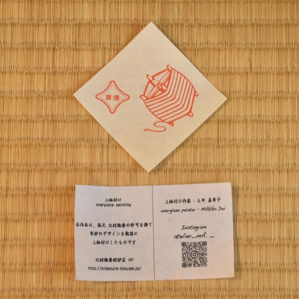 Product tags and cards accompanying the Makiko Doi Musubi Wakakusa matcha bowl, including an orange knot motif, barcode, and QR code.