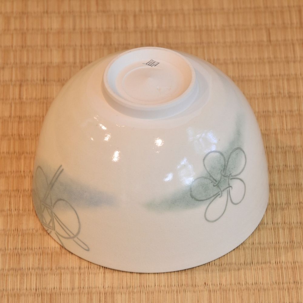 Angled underside view of the Musubi Wakakusa matcha bowl showing green and brown knot motifs around the white exterior and raised foot.