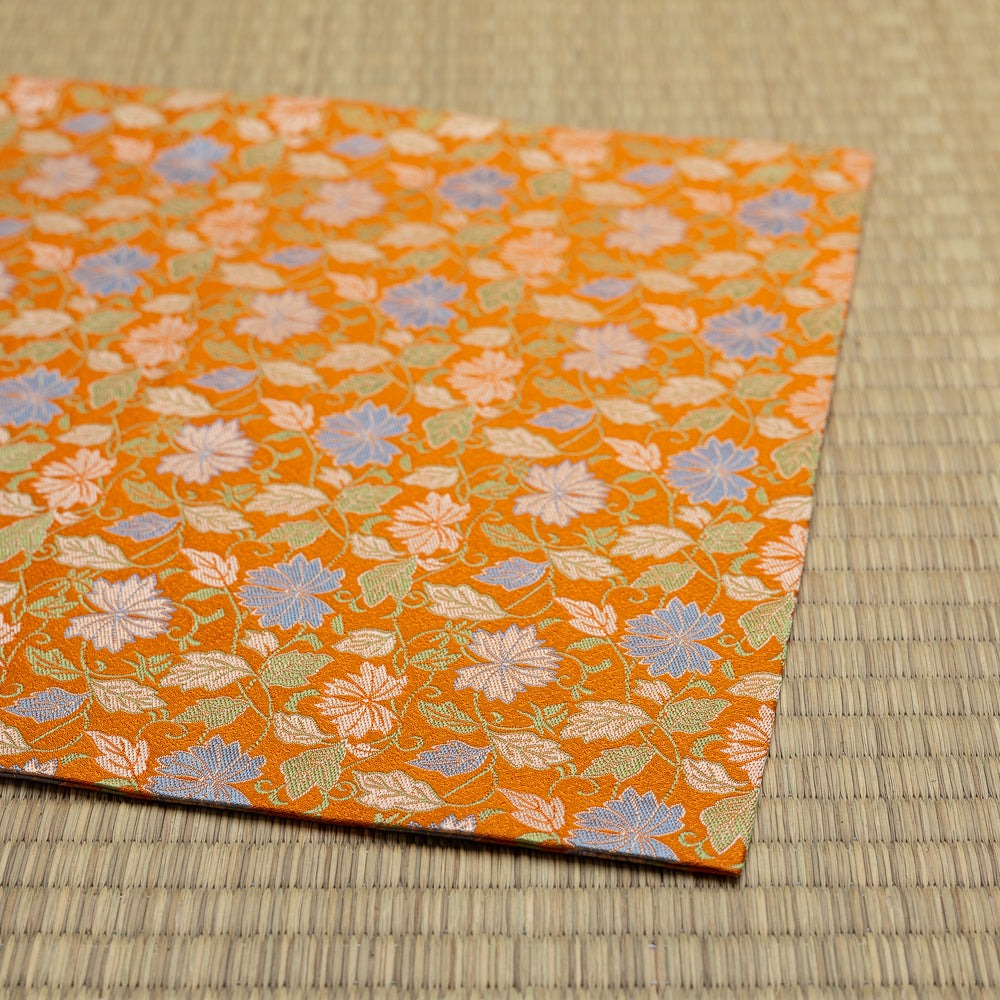 Folded edge of the orange silk dashibukusa showing its hand-sewn construction and repeating chrysanthemum pattern.