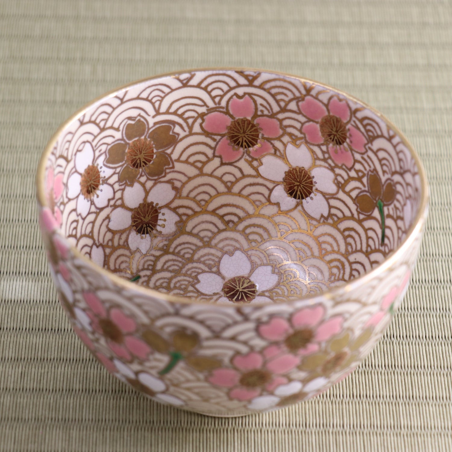 Front angled view of a hand-painted Kyo Ware matcha bowl by Tanaka Bansho, decorated with pink peach blossoms and gold accents over an intricate all-over pattern.