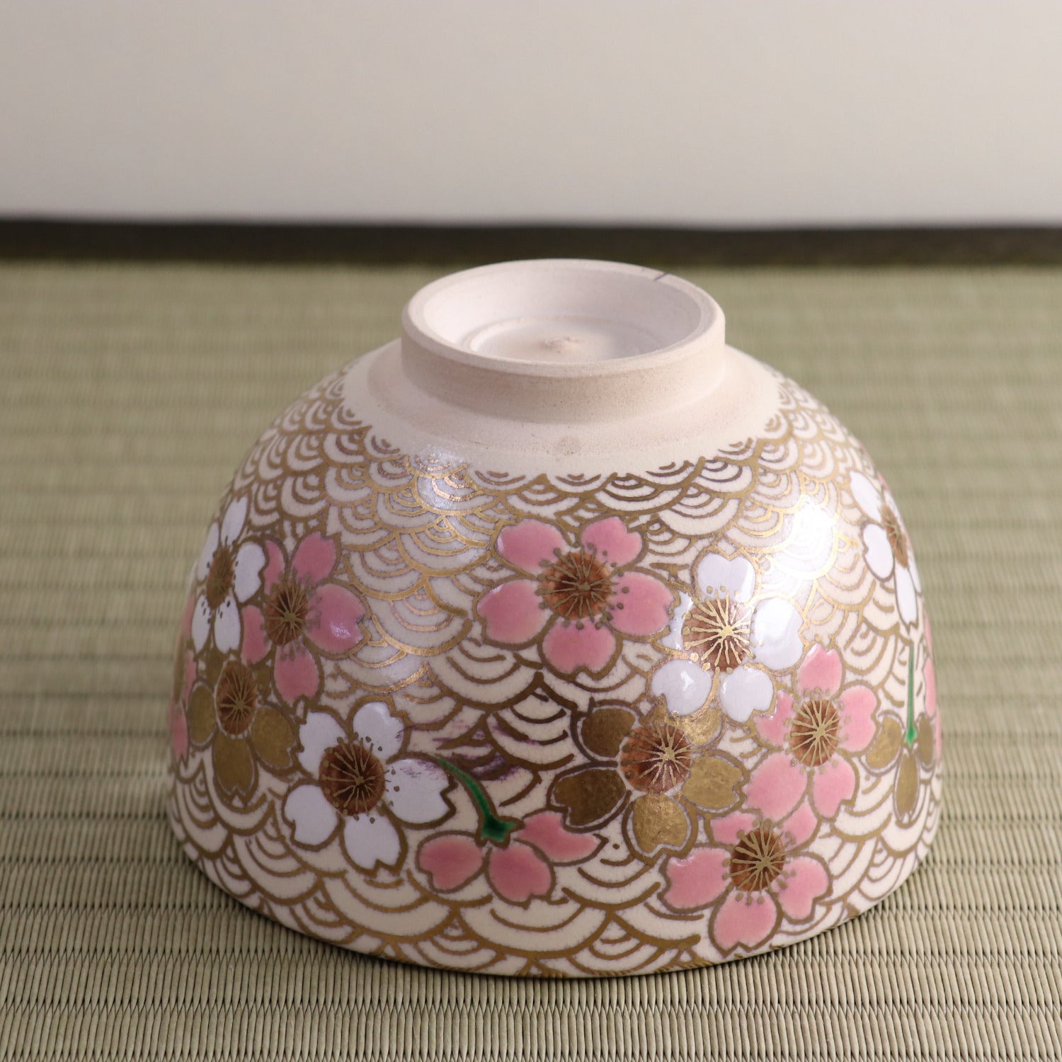Underside view of the hand-painted matcha bowl showing the foot ring and the exterior peach blossom decoration wrapping around the bowl.