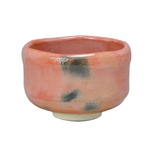Front angled view of a handcrafted Aka Raku Rikyu chawan by Raku Zuisho with a coral-red glaze, smoky black accents, and a pale foot.
