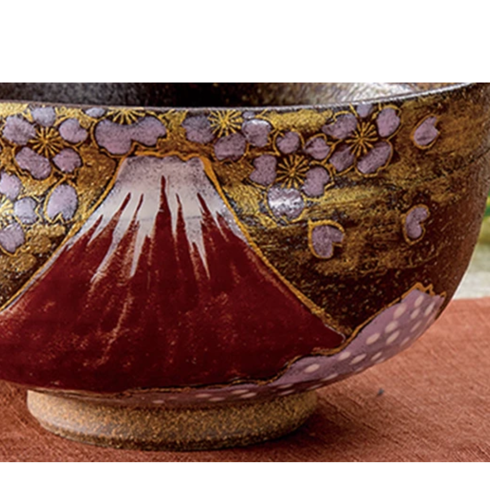 Close-up of the matcha bowl showing the snowcapped crimson Mount Fuji, lavender sakura blossoms, gold-leaf background, and raised foot.