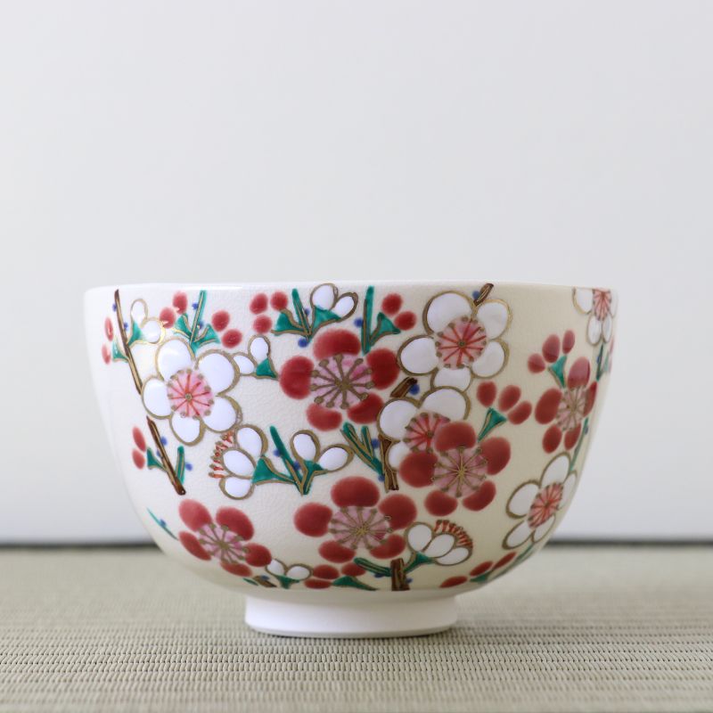 Front view of a hand-painted Kyo Ware matcha bowl covered with red and white plum blossoms, green branches, and delicate gold accents.
