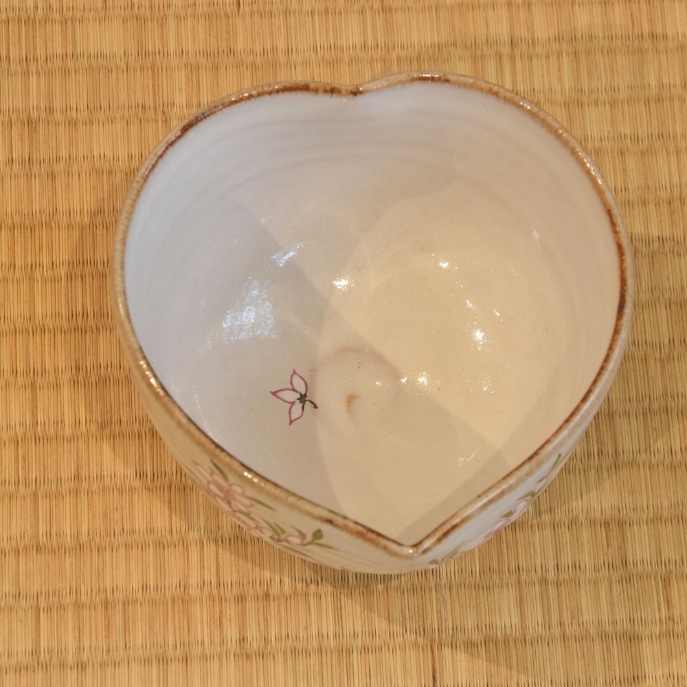 Top view of the petal-shaped katakuchi matcha bowl showing its ivory interior, pointed pouring lip, and a single painted peach petal.