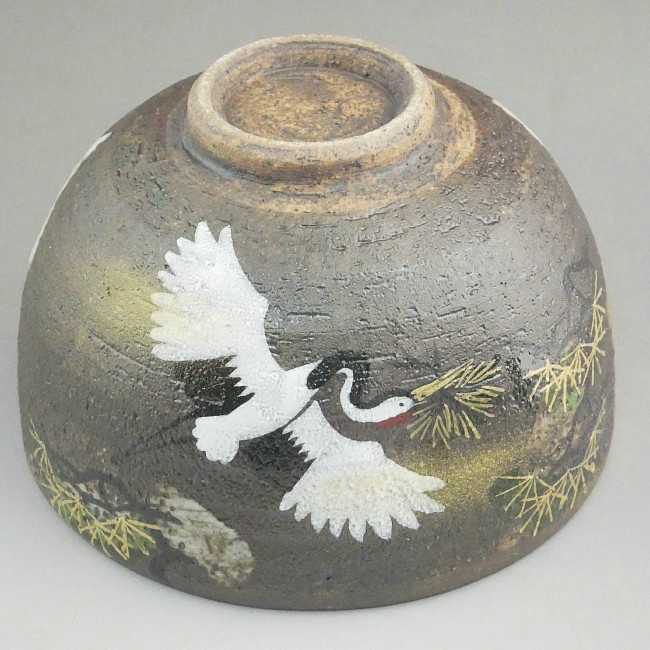 Underside angle of the charcoal-gray Kyo Ware matcha bowl showing its exposed foot and white crane decoration wrapping around the exterior.