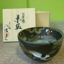 Sakata Yahata crane and plum blossom matcha bowl displayed with its box and accompanying papers against a green background.