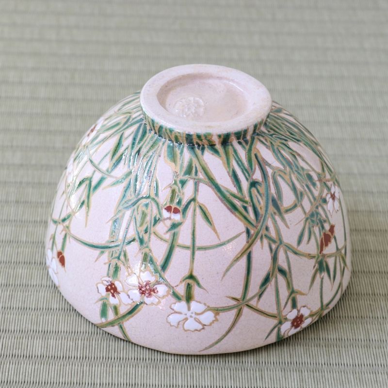 Underside view of the Shisen Asano Nadeshiko chawan showing the raised ceramic foot and dense green grass and floral decoration around the exterior
