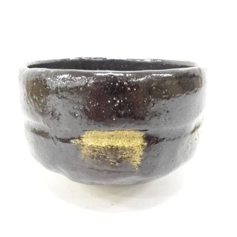 Side view of the Shoraku Sasaki Sennen no Midori Black Raku chawan showing its deep glossy black glaze, irregular hand-formed shape, and gold-toned accent
