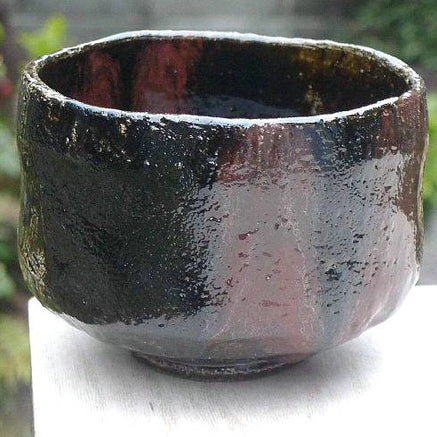Angled front view of the Kakuyo Black Raku matcha bowl showing its irregular rim, rounded form, and reddish-brown glaze variation.