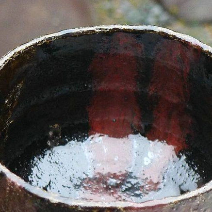 Top view of the Kakuyo matcha bowl showing its deep black interior with copper-red and dark plum-toned firing effects.
