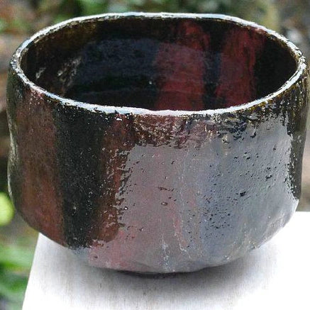 Left-side view of the Kakuyo Black Raku matcha bowl highlighting its softly irregular form and shifting black and bronze-toned glaze.