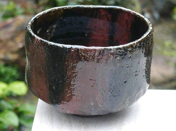 Left-side view of the Kakuyo Black Raku matcha bowl highlighting its softly irregular form and shifting black and bronze-toned glaze.