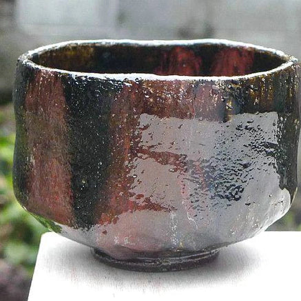 Right-side view of the Shuraku Kiln Black Raku bowl showing glossy black glaze and a broad copper-red surface variation.