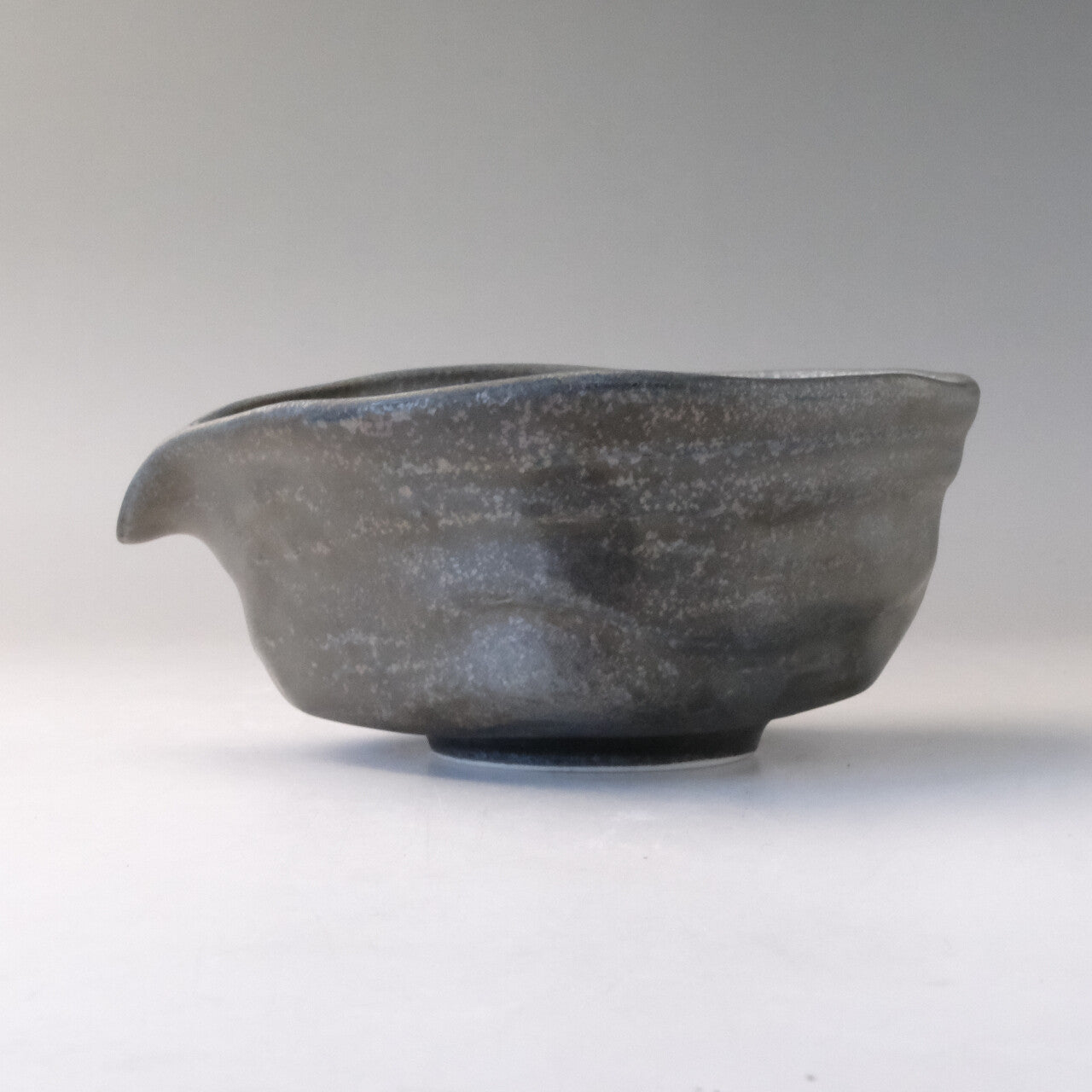 Left-side profile of the smoky silver-gray matcha bowl showing the pouring spout, low foot, and rustic glaze variations.