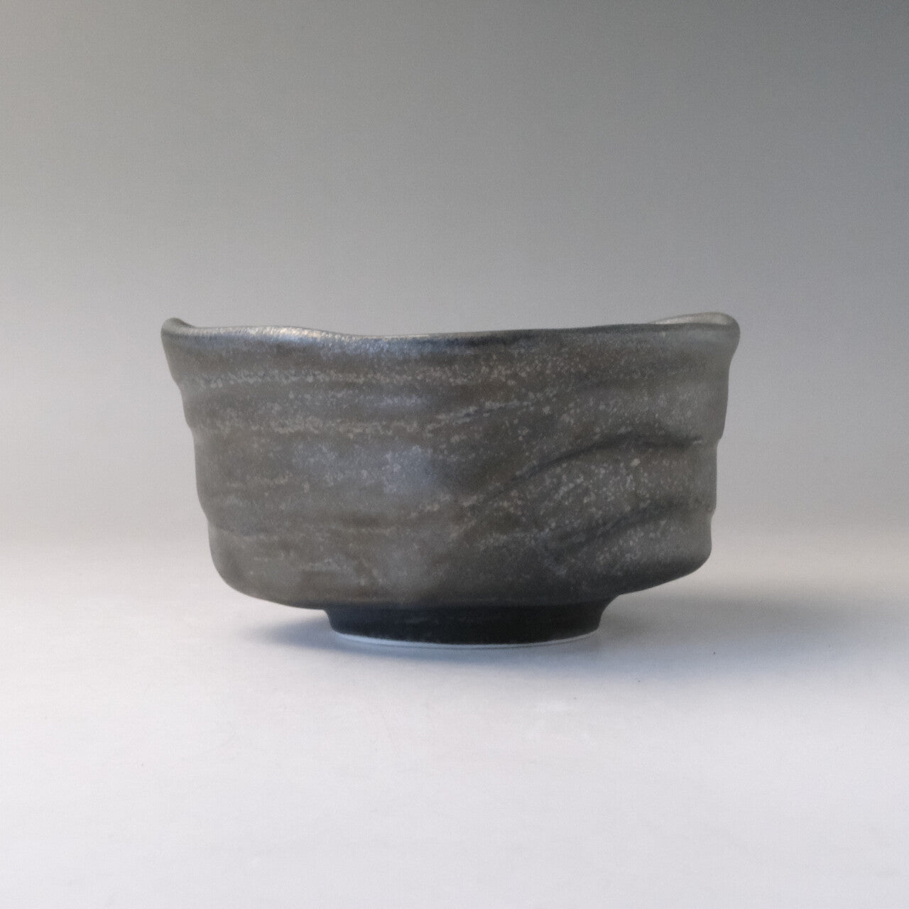 Rear profile of the Mino Ware matcha bowl showing its low rounded form, horizontal ridges, and smoky textured glaze.