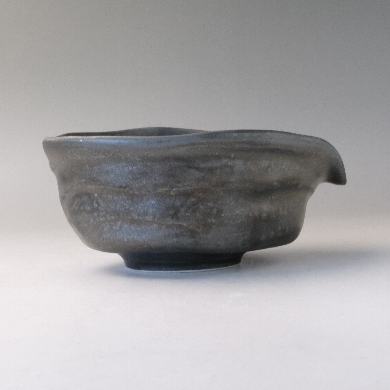 Right-side profile of the silver-gray katakuchi bowl showing the pouring spout extending from its softly irregular rim.