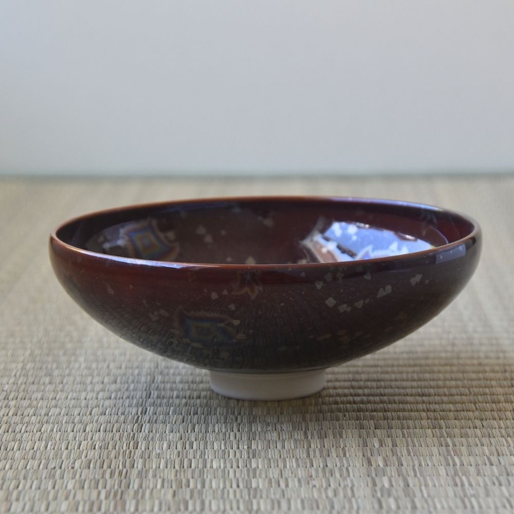 Side profile of the Touan Hoshi-Kessho flat matcha bowl showing its wide low form, wine red glaze, and white ceramic foot