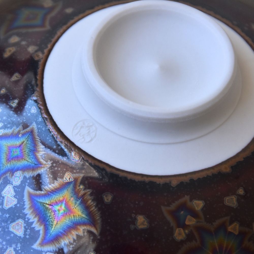 Close-up of the Touan Hoshi-Kessho matcha bowl foot showing the white ceramic base and colorful star-like crystal formations in the wine red glaze