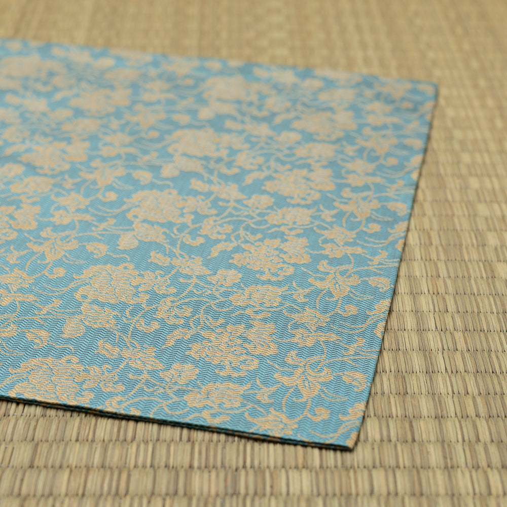 Folded edge of the hand-sewn dashibukusa showing its turquoise ground and continuous gold-toned vine pattern.