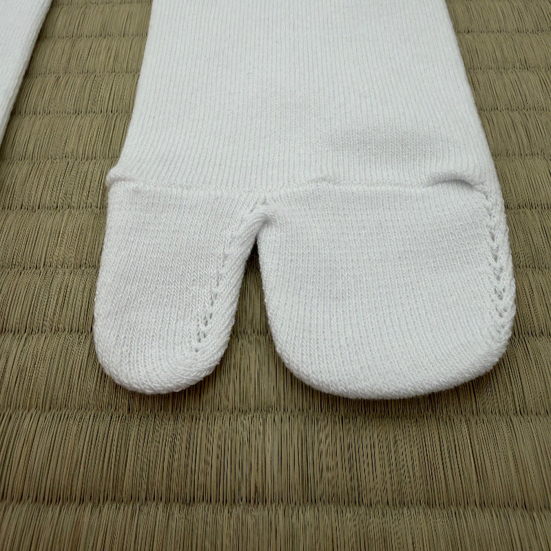 A close-up of a white tabi sock with its split toe separated, laid flat on a woven straw mat.