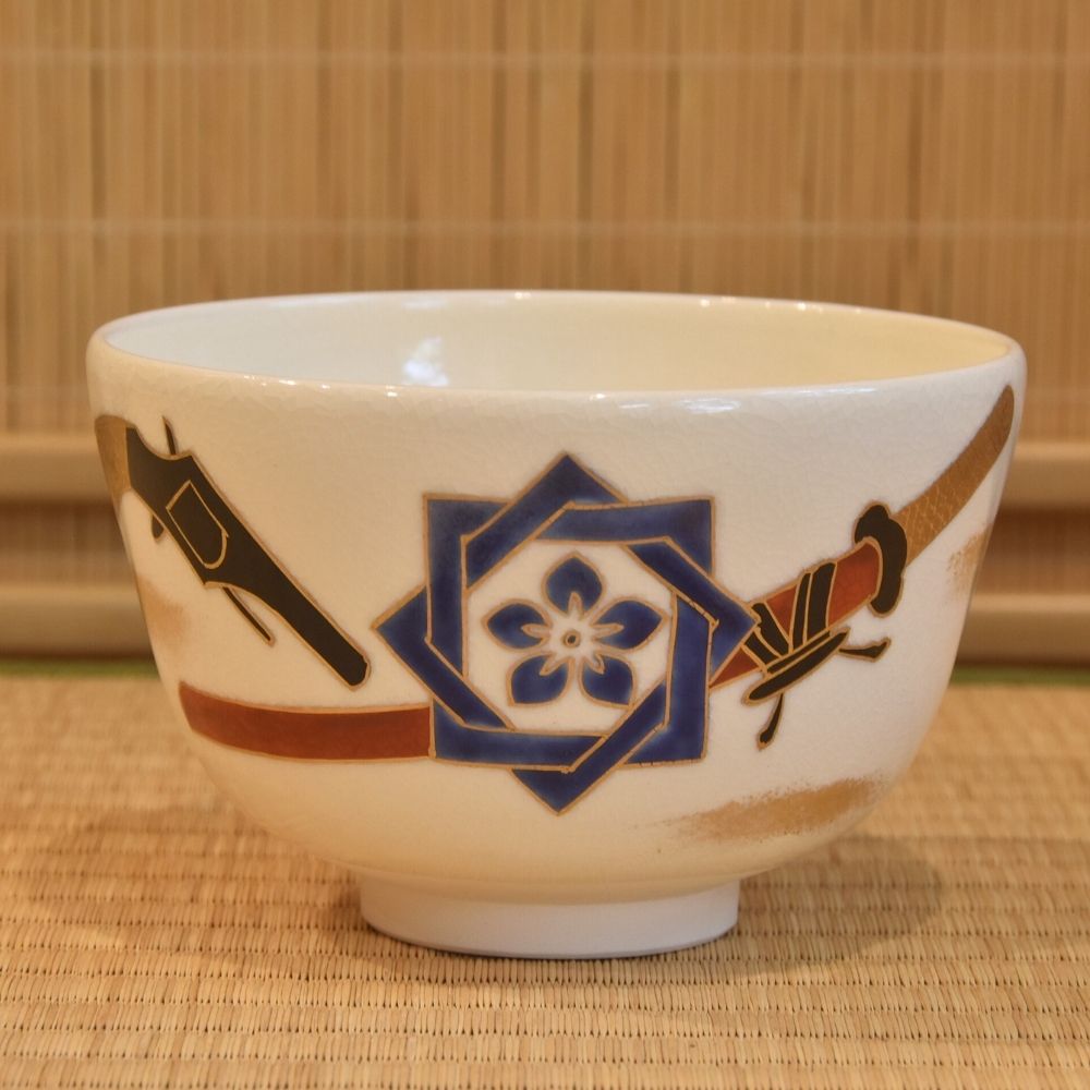 Front view of a hand-painted Kyo Ware matcha bowl by Zensho Yamaoka featuring Ryoma Sakamoto's blue family crest and pistol motifs.