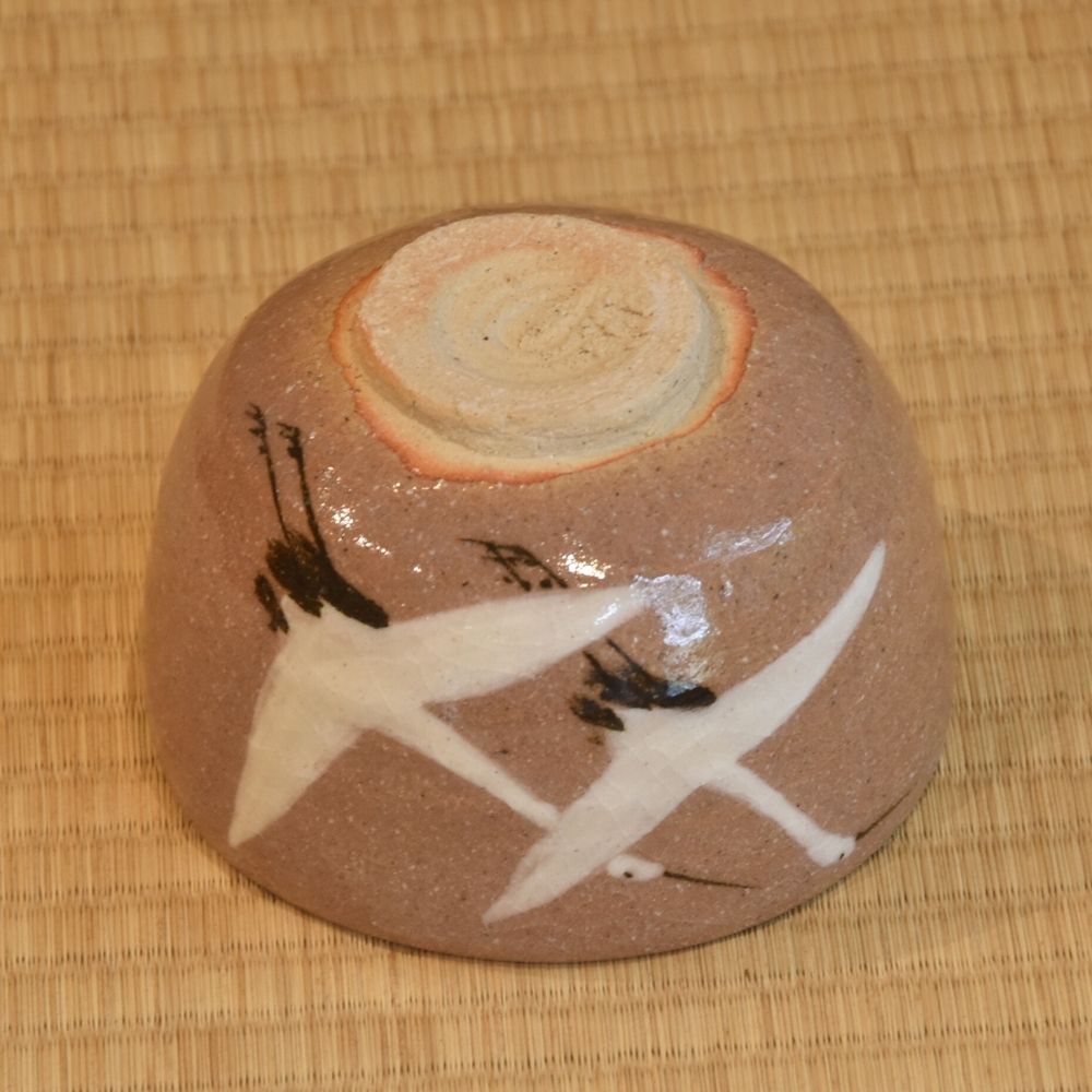 Angled underside view of the Dancing Cranes matcha bowl showing the rounded body, crane motifs, and exposed circular foot.