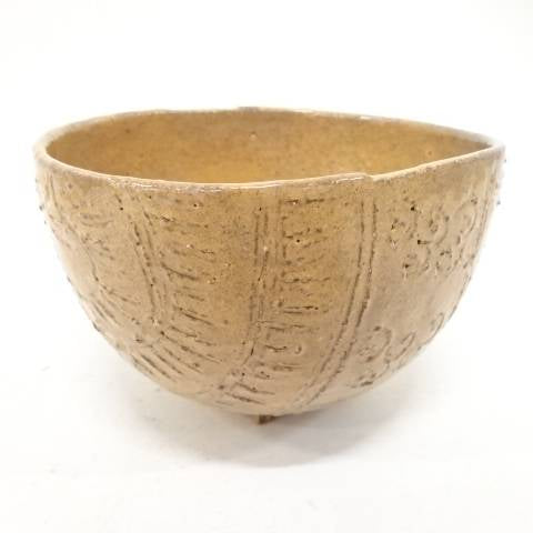 Front view of the Zuiho Ono Hagi chawan showing its rounded tawara form, warm amber glaze, and carved straw-bale texture.