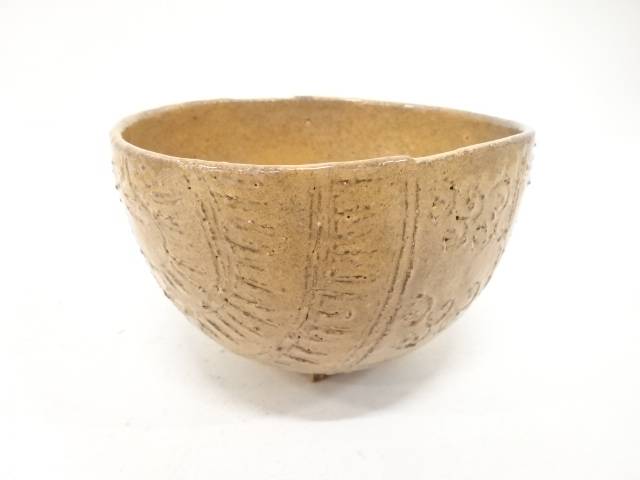 Front view of the Zuiho Ono Hagi chawan showing its rounded tawara form, warm amber glaze, and carved straw-bale texture.
