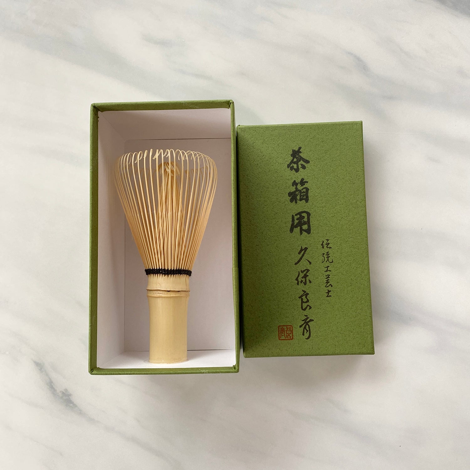 A white bamboo whisk, Shirotake Takayama Chasen Nodate, displayed in an open green box with Japanese characters.
