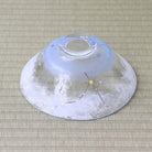 A clear glass bowl with a white and light blue painted design and small yellow celestial dots, photographed from above on a beige woven mat.