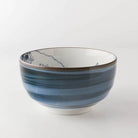 A ceramic bowl with a blue and white striped pattern and delicate hand-painted mountain details inside, set against a plain white background.