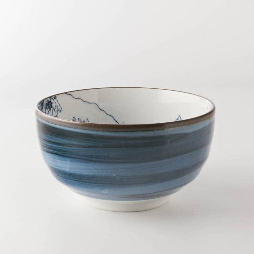 A ceramic bowl with a blue and white striped pattern and delicate hand-painted mountain details inside, set against a plain white background.