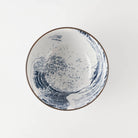 A white ceramic bowl featuring a blue wave illustration inspired by 'The Great Wave off Kanagawa', with a thin brown rim, shown from a top-down view on a light gray background.