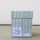 A square light green and white textured box with Japanese characters printed on a white label, placed on a woven mat against a plain light background.