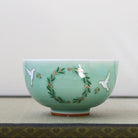 A light green ceramic bowl with hand-painted white doves and a green wreath design with gold accents, resting on a textured surface against a neutral background.