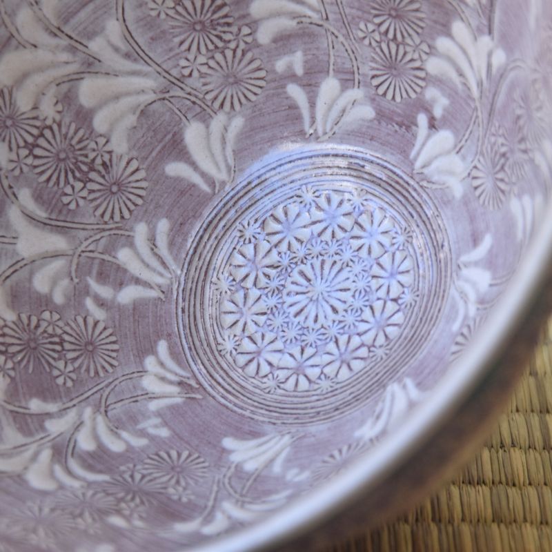 Close-up of a ceramic bowl with intricate floral patterns on a woven surface.