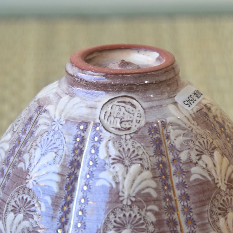 Decorative ceramic vase with intricate patterns and a visible brand label on a beige background