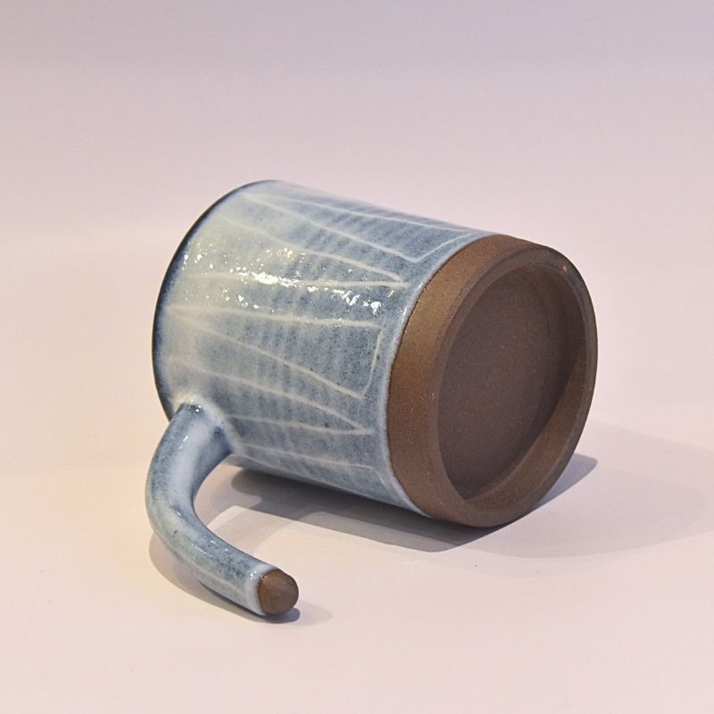 Cylindrical ceramic mug with blue glaze and brown base on a white background