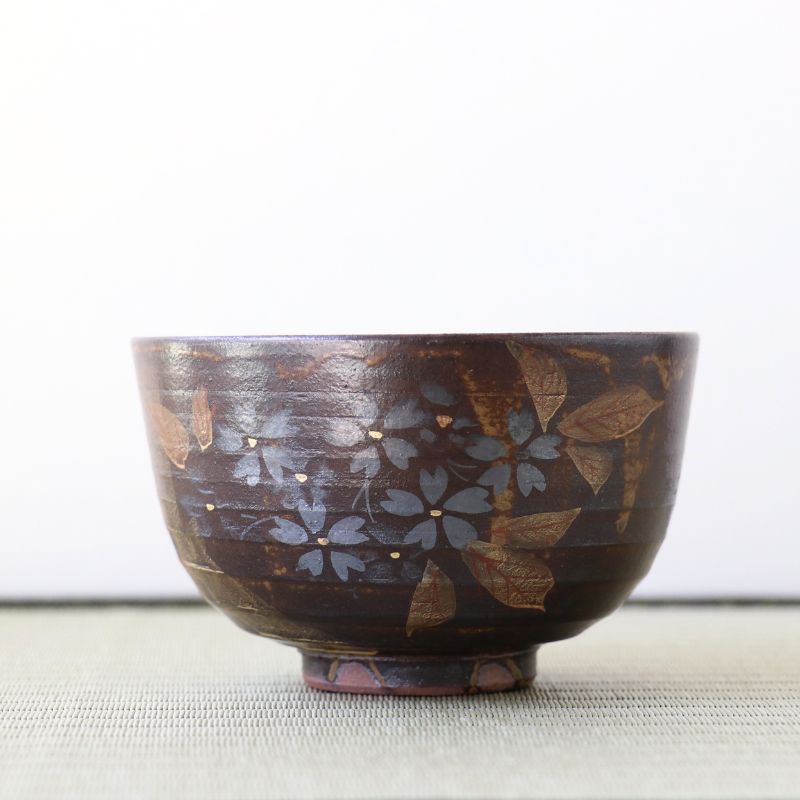 A dark brown ceramic bowl with hand-painted blue-gray cherry blossoms and gold leaf accents, set against a plain white background.