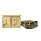 Ceramic bowl with gold leaf design next to a wooden box with Japanese text on a white background